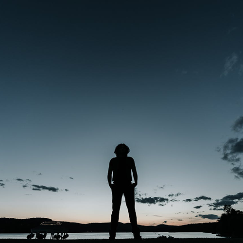 Silhuetten av en person med en sjö och en bara lite ljus himmel i bakgrunden.